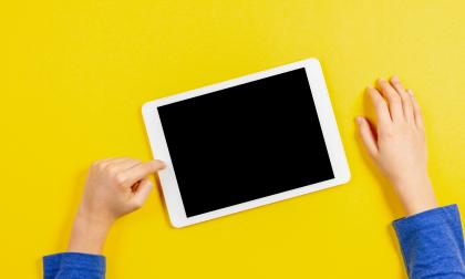 Kid hands with tablet computer on yellow background.