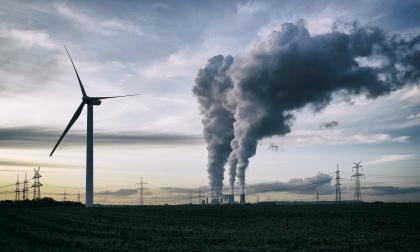 Single wind turbine, a coal burning power plant with pollution and electricity pylons in the background.