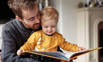 Cropped shot of an adorable little boy reading a book while sitting with his father at home