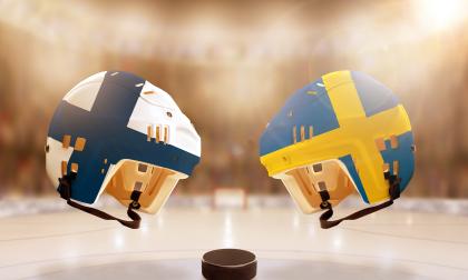 Low angle view of hockey helmets with Finland and Sweden flags painted and hockey puck on ice in brightly lit stadium background. Concept of intense rivalry between the two hockey nations.