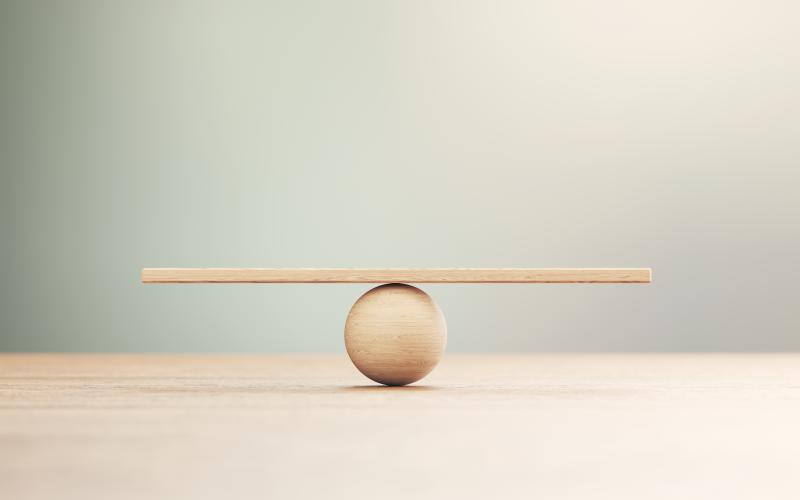 Wooden seesaw scale sitting on wood surface in front of defocused background. Balance concept.