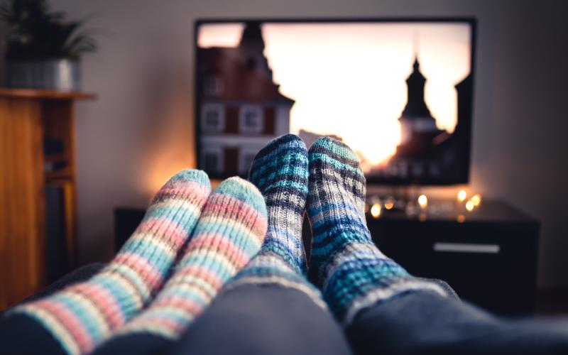 Couple with socks and woolen stockings watching movies or series on tv in winter. Woman and man sitting or lying together on sofa couch in home living room using online streaming service in television