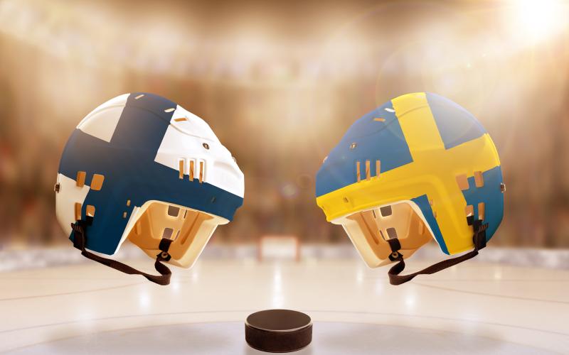 Low angle view of hockey helmets with Finland and Sweden flags painted and hockey puck on ice in brightly lit stadium background. Concept of intense rivalry between the two hockey nations.