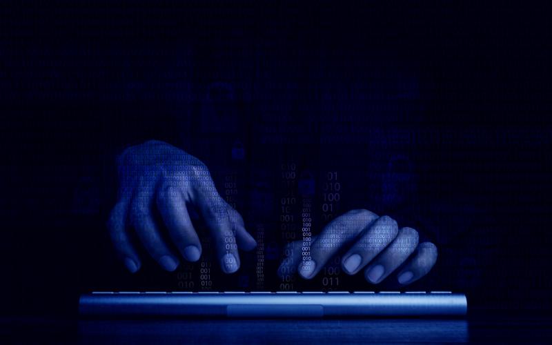 Cyberattack and internet crime, hacking and malware concepts. Digital binary code data numbers and secure lock icons on hacker' hands working with keyboard computer on dark blue tone background.