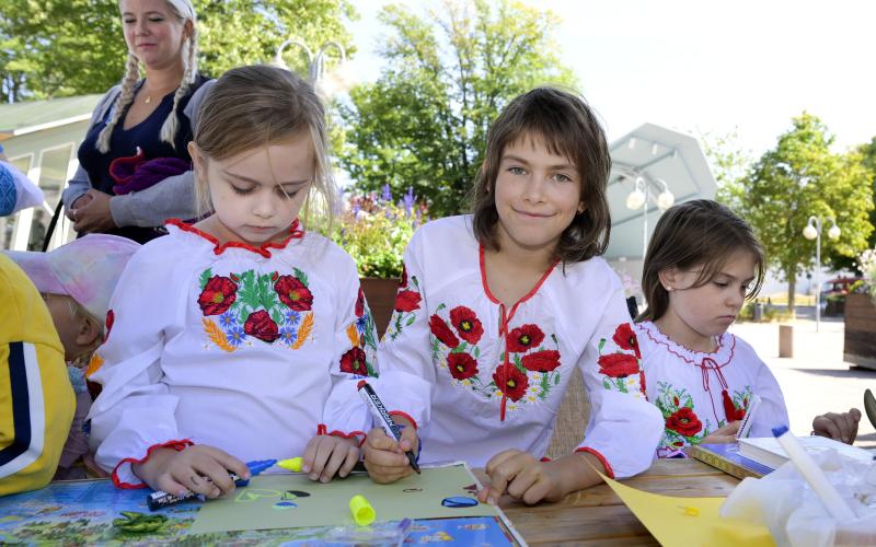 Sofiia Aziri samt Darya och Anastasiia Dubitska målar vid ett av torgborden.