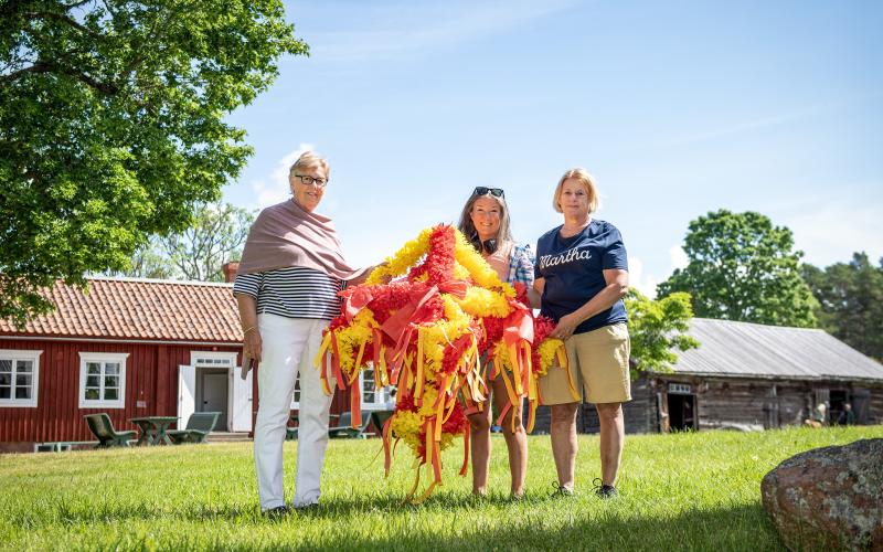 Marthorna Anna-Lisa Johansson, Lina Antman och Ann Carlsson visar upp en av kronorna som ska pryda midsommarstången på Jan Karlsgården.