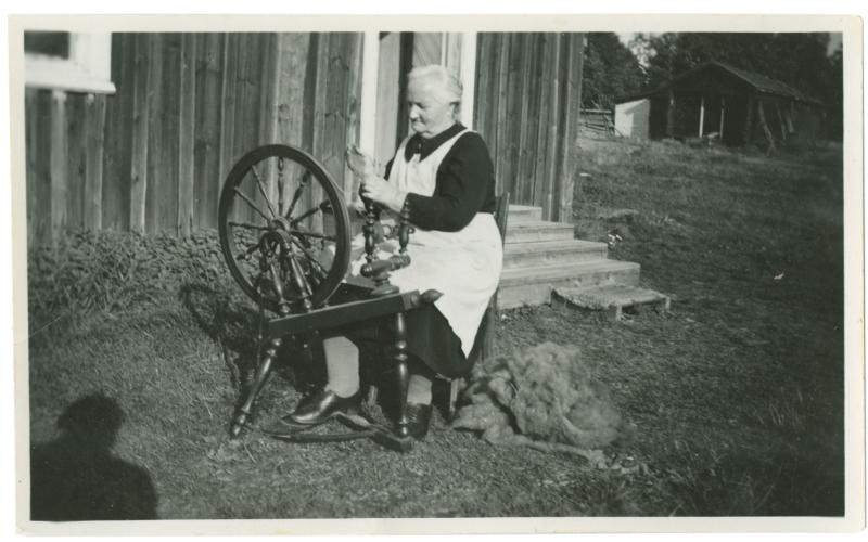 Hanna Mattsson (f. 1884) spinner garn framför bagarstugan vid Södergårds i Klemetsby, Lumparland. Foto ur Elvi Knahpes samling, Önningebymuseet.